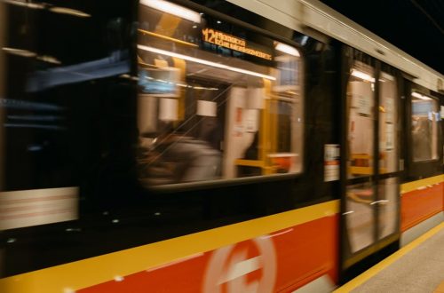 A blurred metro train speeds through an underground station with passengers on board.